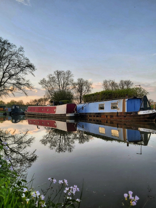 Pretty colourful canal boats with trees and flowers reflected in the water