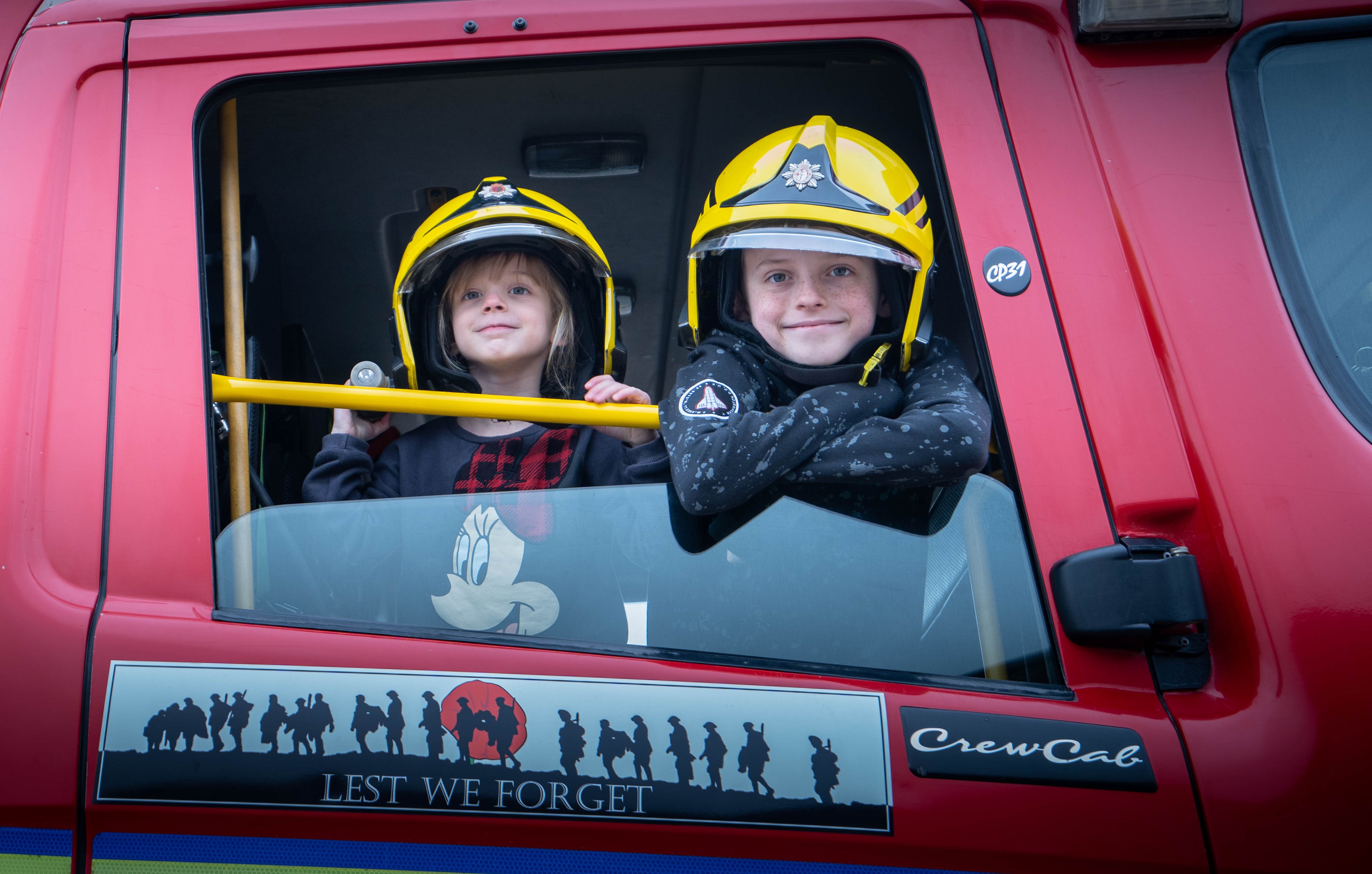 Two smiling children in a fire engine wearing firefighter helmets