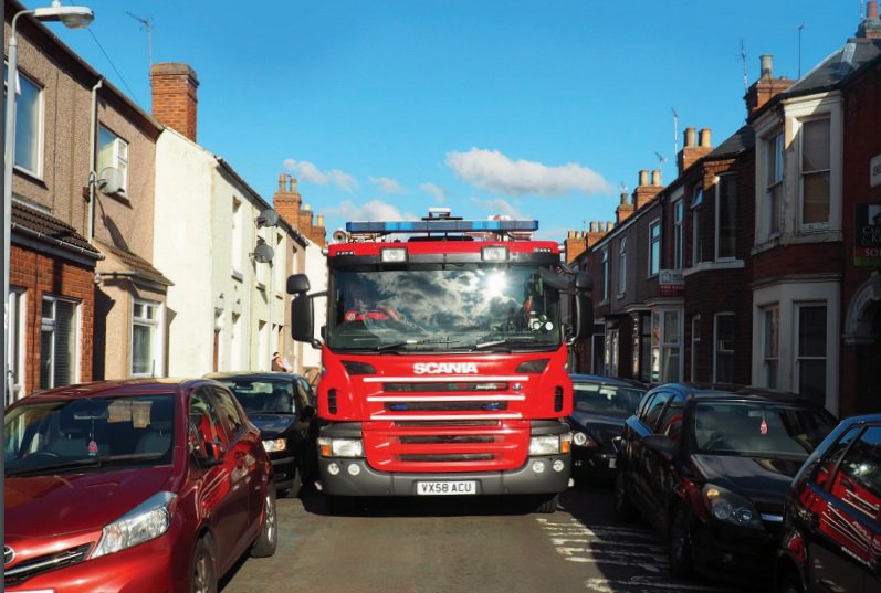A fire engine trying to access a street with cars parked down both sides