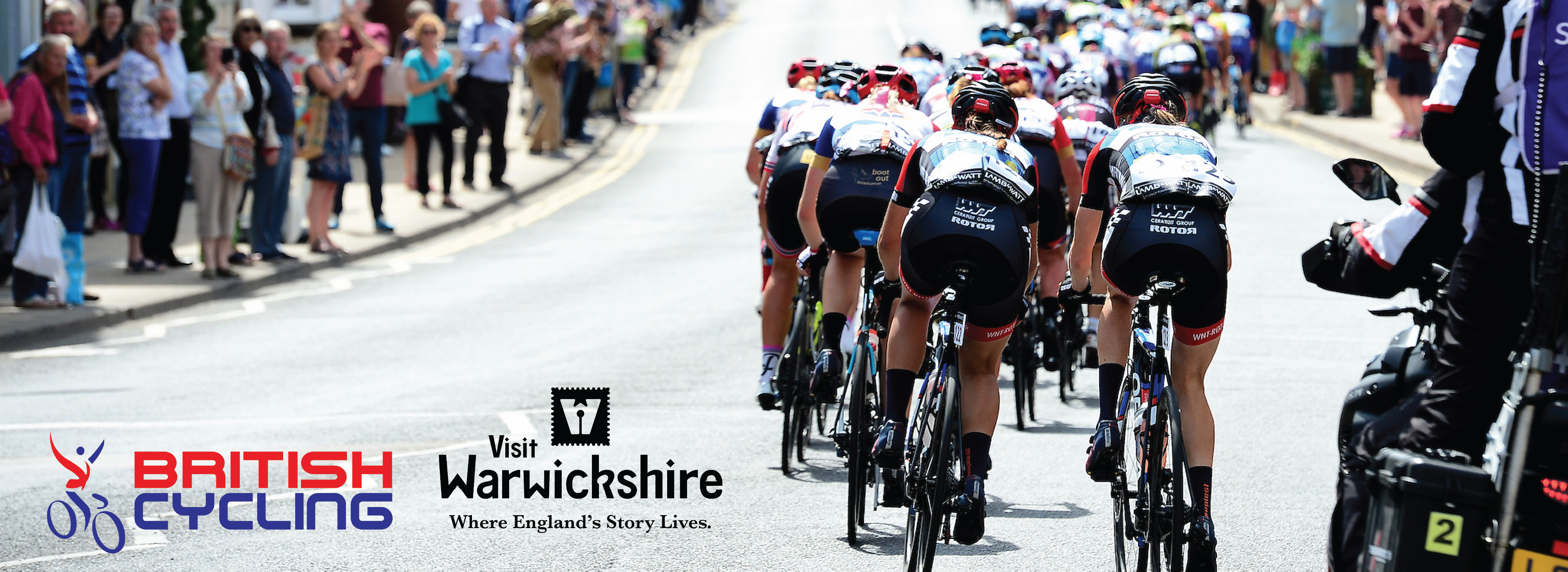 Photo of cyclists in a previous Tour of Britain race with crowds lining the streets, cheering.
