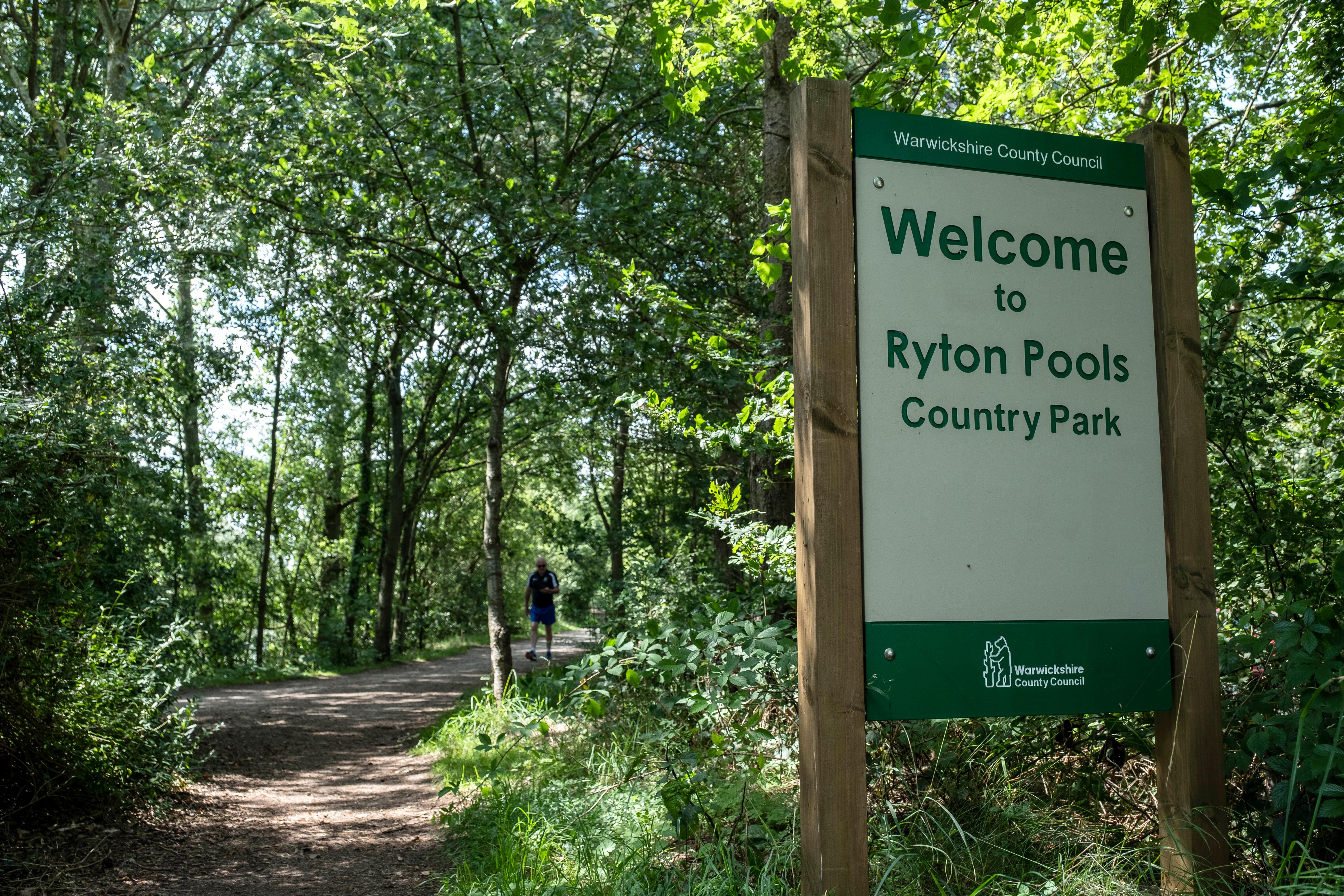 A photograph of a sign reading "welcome to Ryton Pools Country Park". The sign is surrounded by woodland, with a path visible in the foreground.