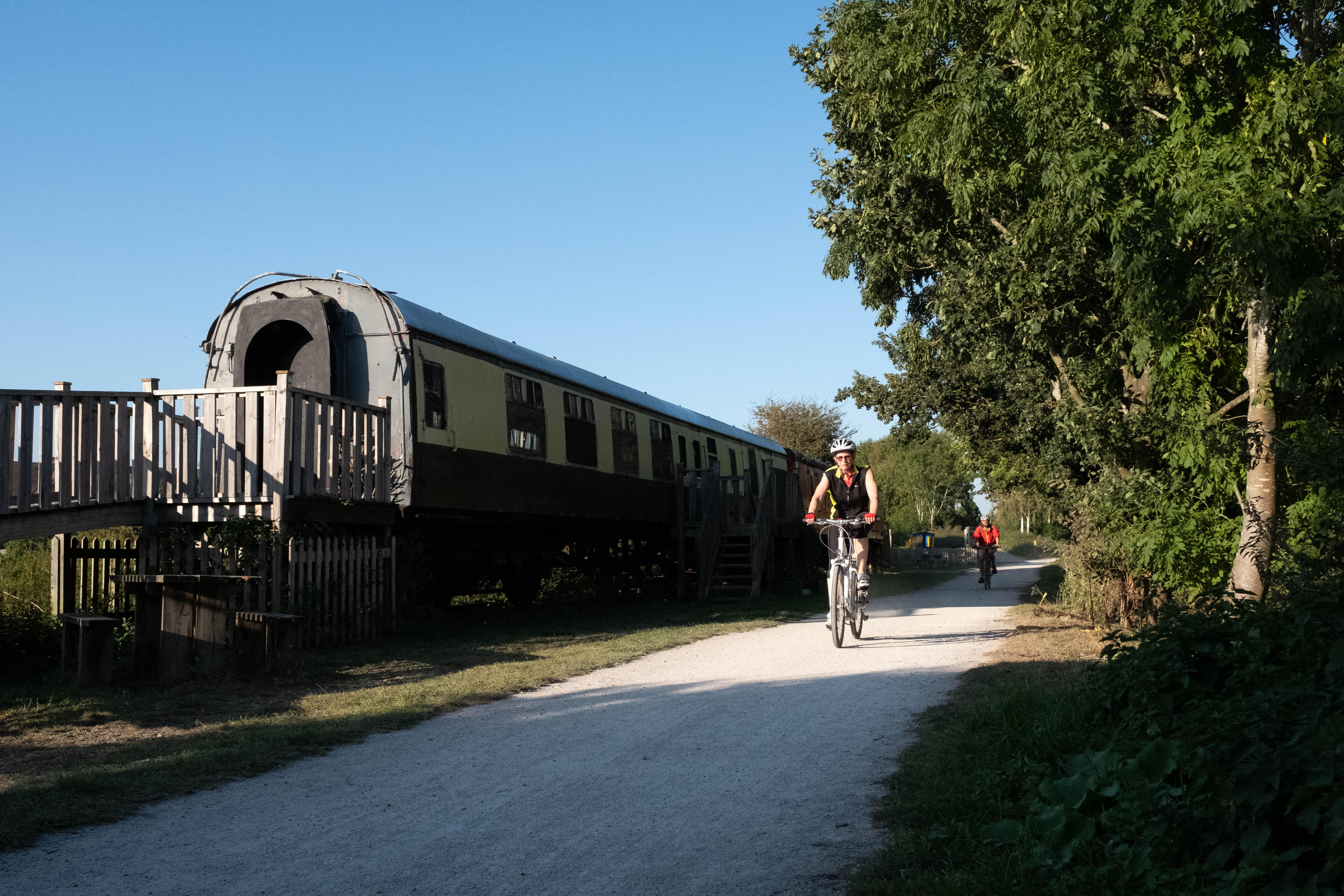 A pathway at Stratford Greenway. On the path, there is a cyclist heading towards the camera man. On the side of the path is an old railway carriage.