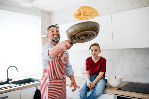Dad flipping pancake with son watching on
