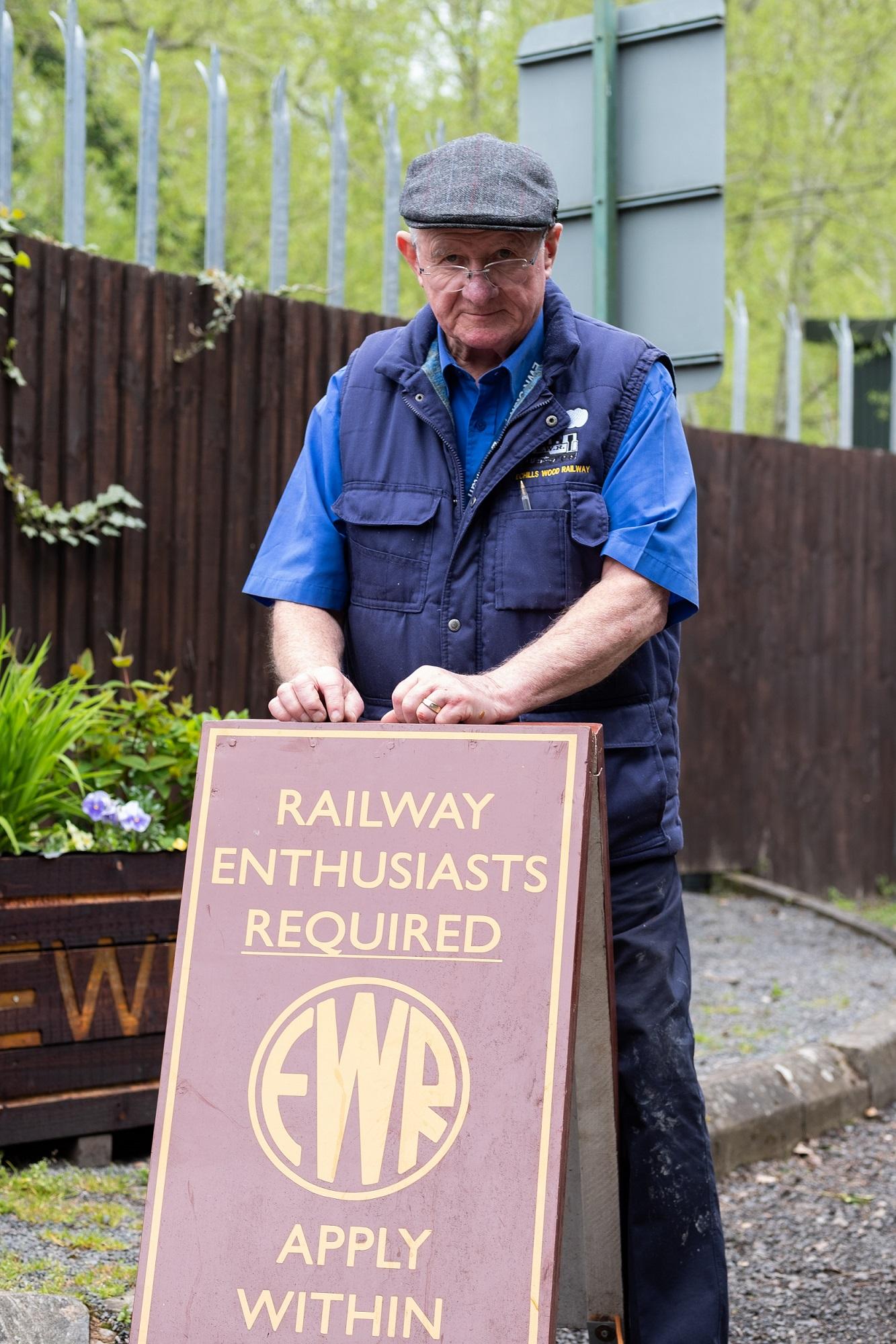 Photograph of Jeff Stevens, Secretary of the Echills Wood Railway, standing in front of a sign which invites volunteers to join.