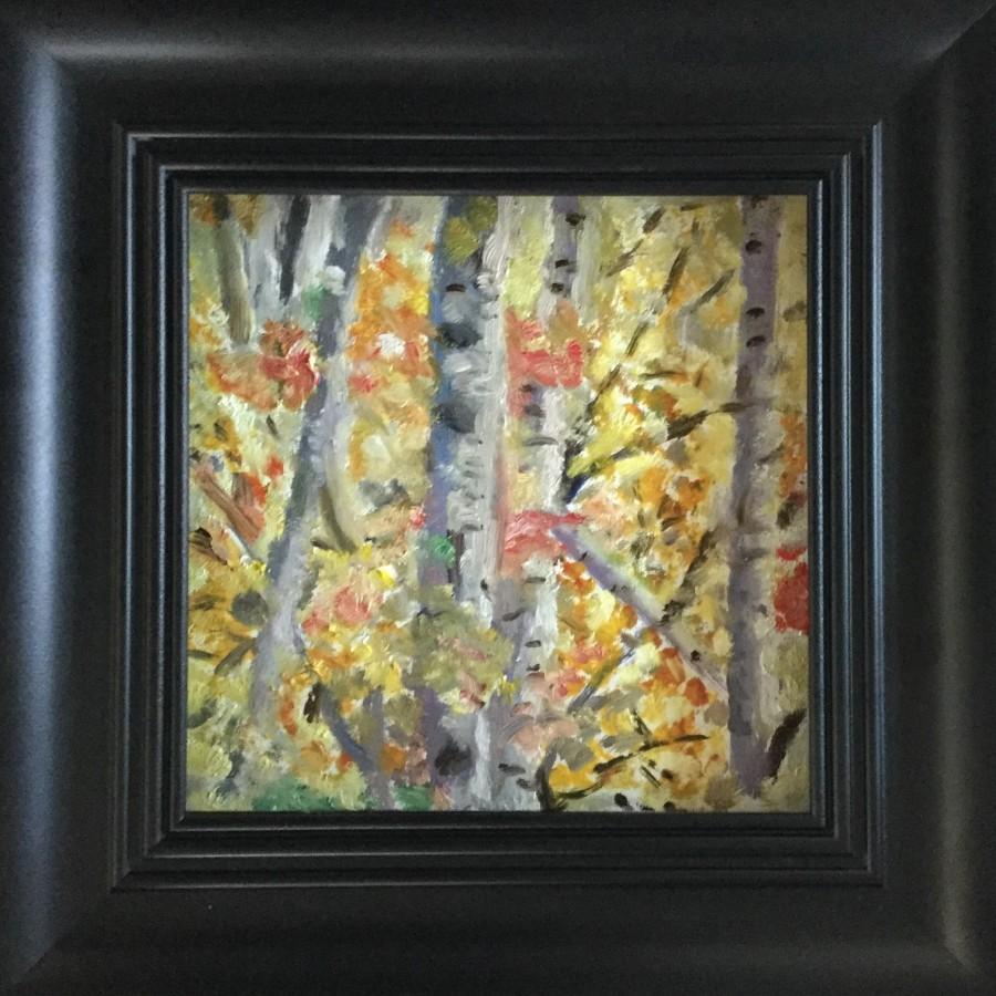 A black framed painting of grey thin tree trunks with red, orange and yellow leaves on the tree branches and trunks.