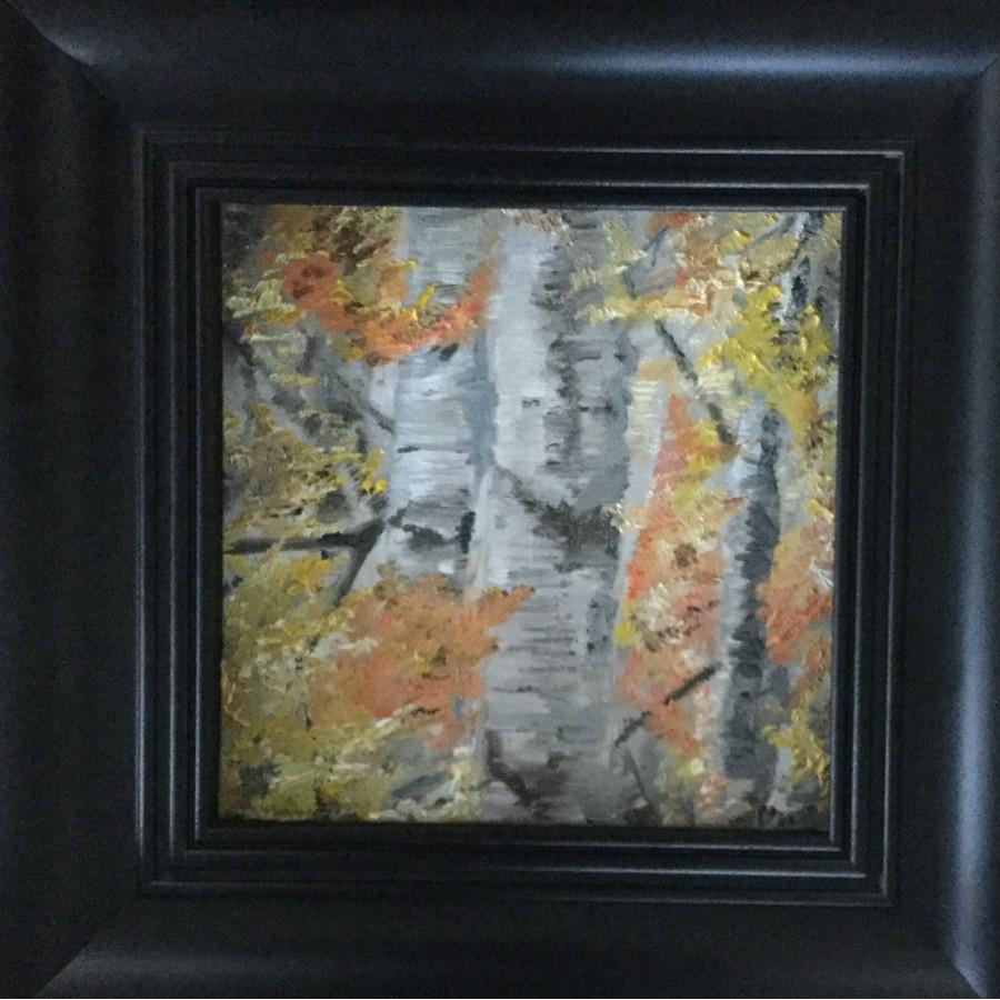 A black framed painting of grey tree trunks with red, orange and yellow leaves on the tree branches.