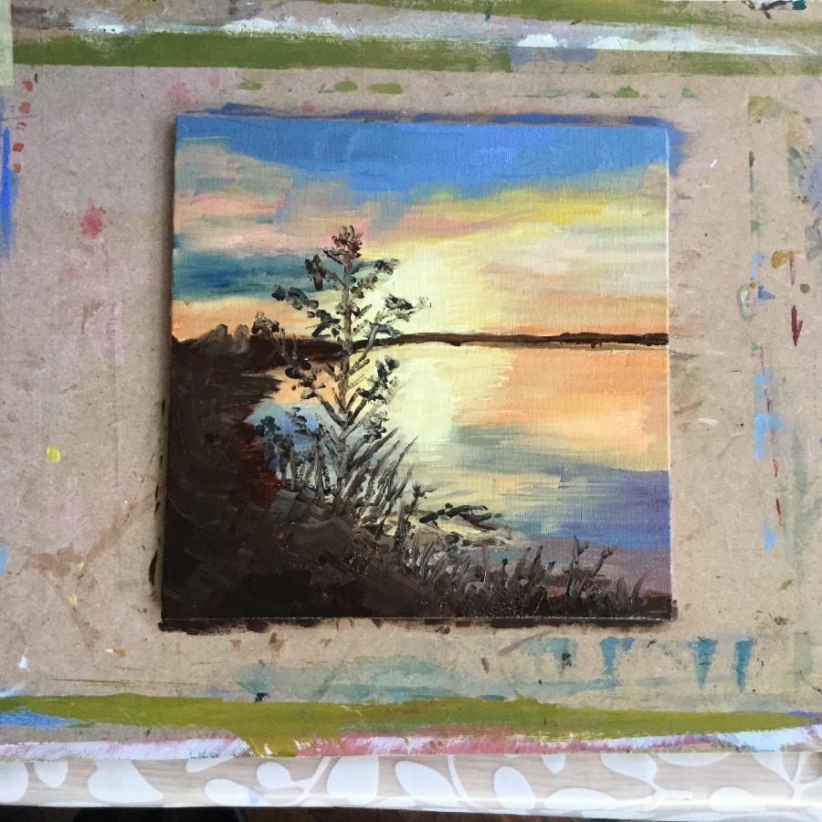 painting of an orange and yellow sunset reflected across a lake. On the left of the painting are some small tree branches.