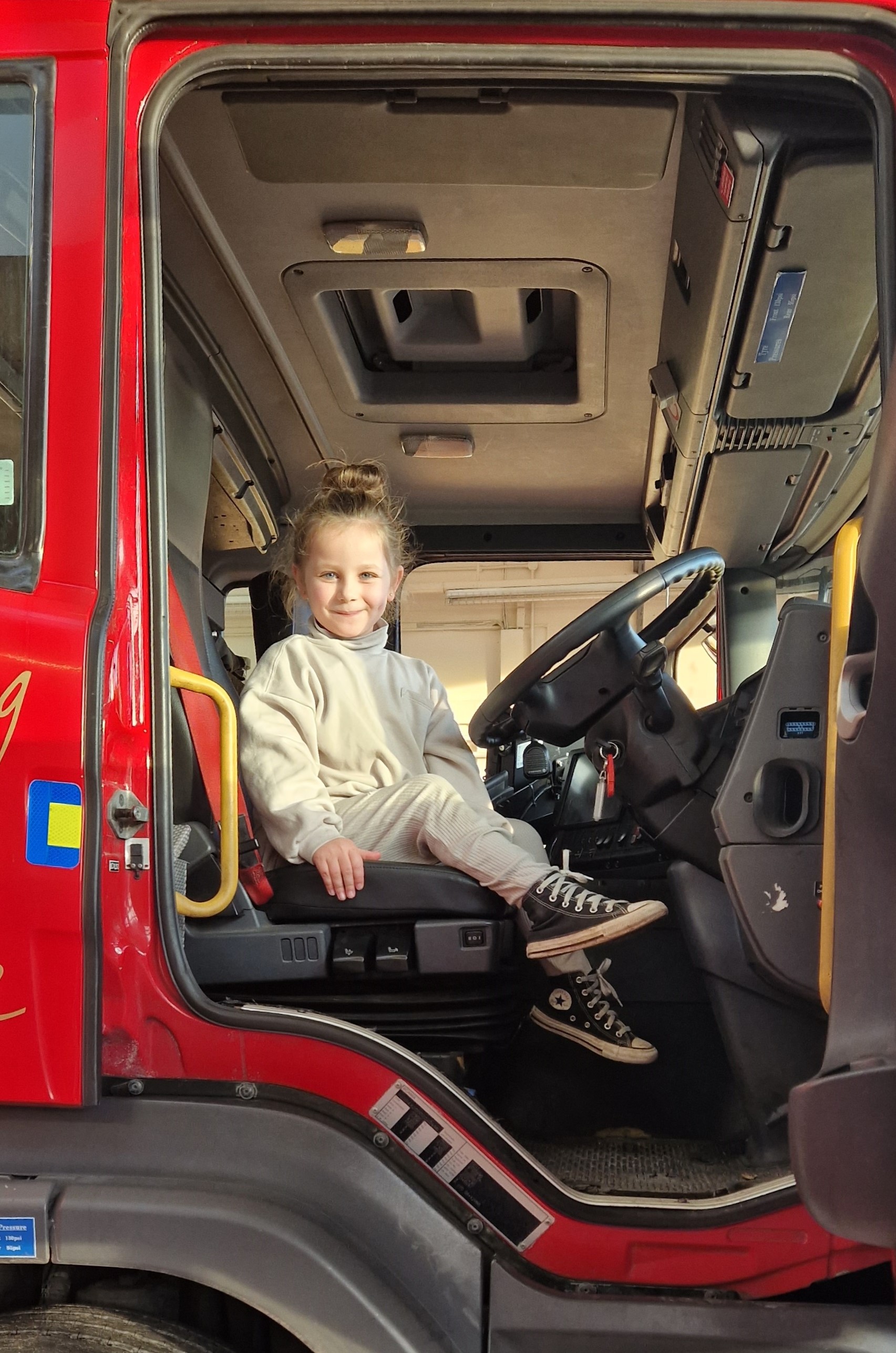 A smiling young girl looks down from the driver's seat of a fire engine