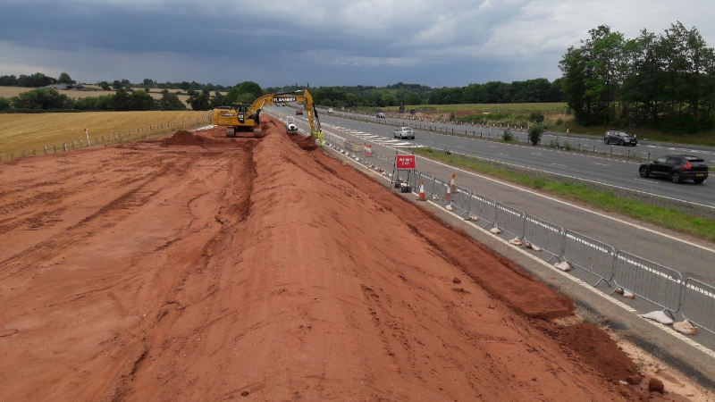 Depicting construction digger creating earthworks alongside one of the junction slip roads.