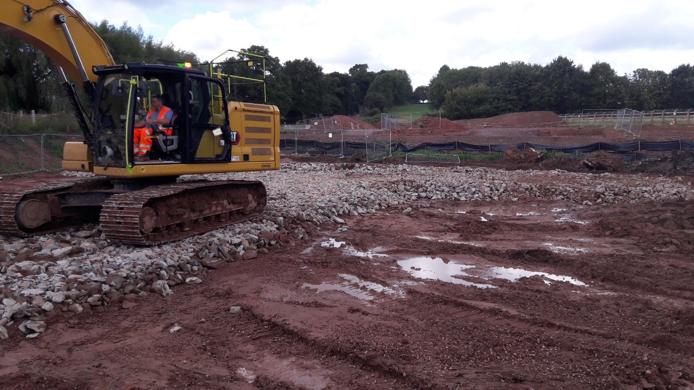 Photograph showing a yellow digger building the rock foundations ready for a road surface to be laid on top.