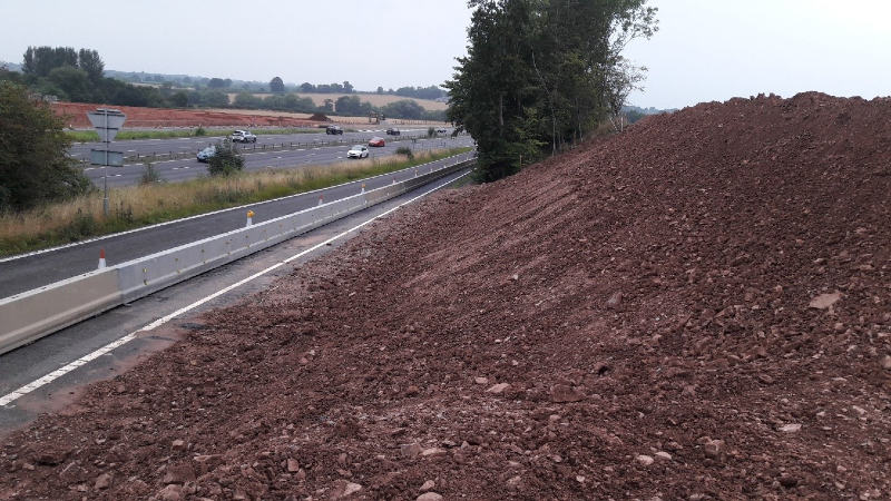 Depicting a long mound of earth being constructed as part of the new earthworks for the slip road to the new junction