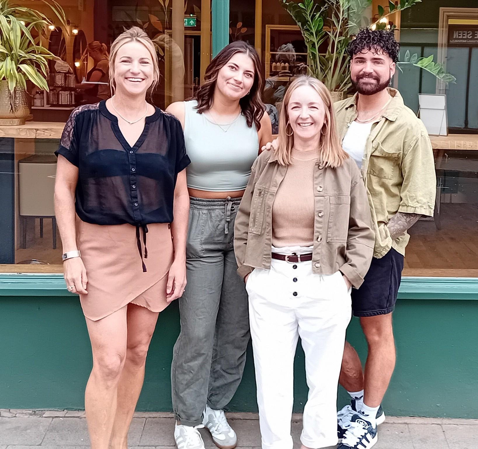 Four people standing in front of a hairdressers' salon.