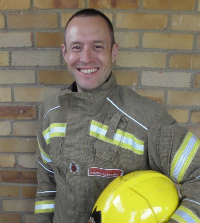 Matthew Brand holding his helmet, wearing his fire fighting uniform.