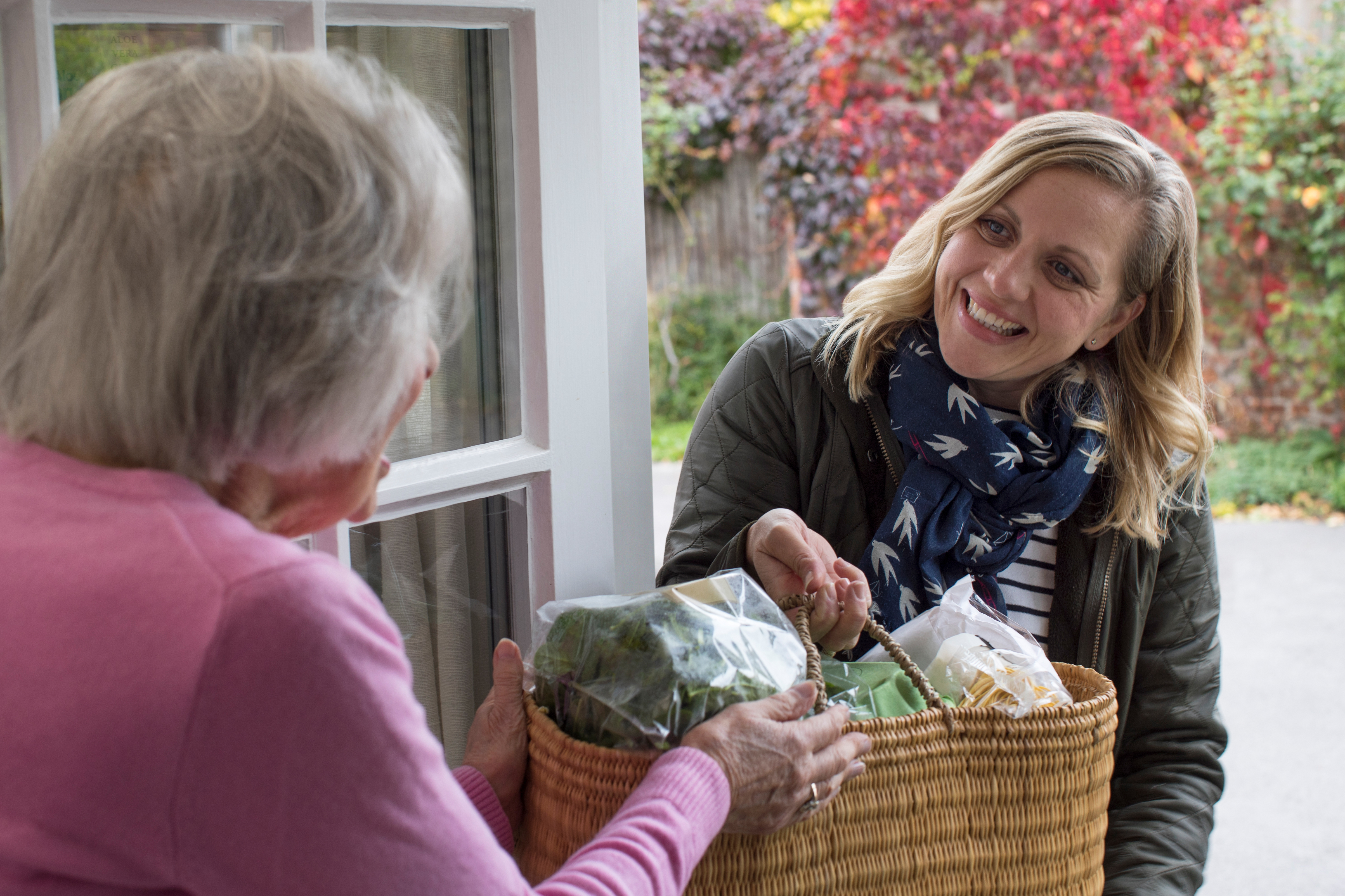 A woman handing a bag of groceries to an older woman