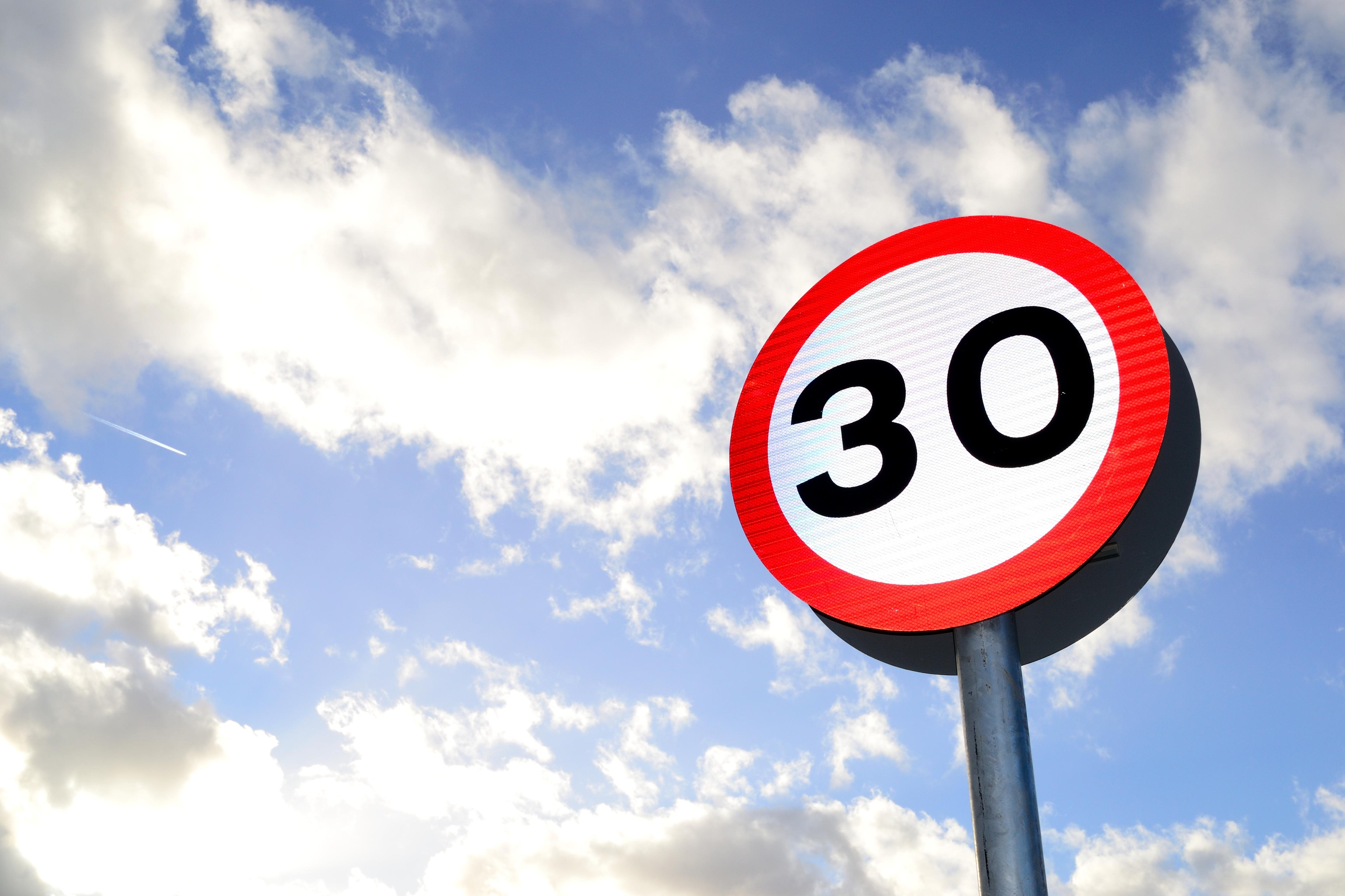 A photograph of a 30 miles-per-hour speed limit sign, with a blue sky with some clouds in the background