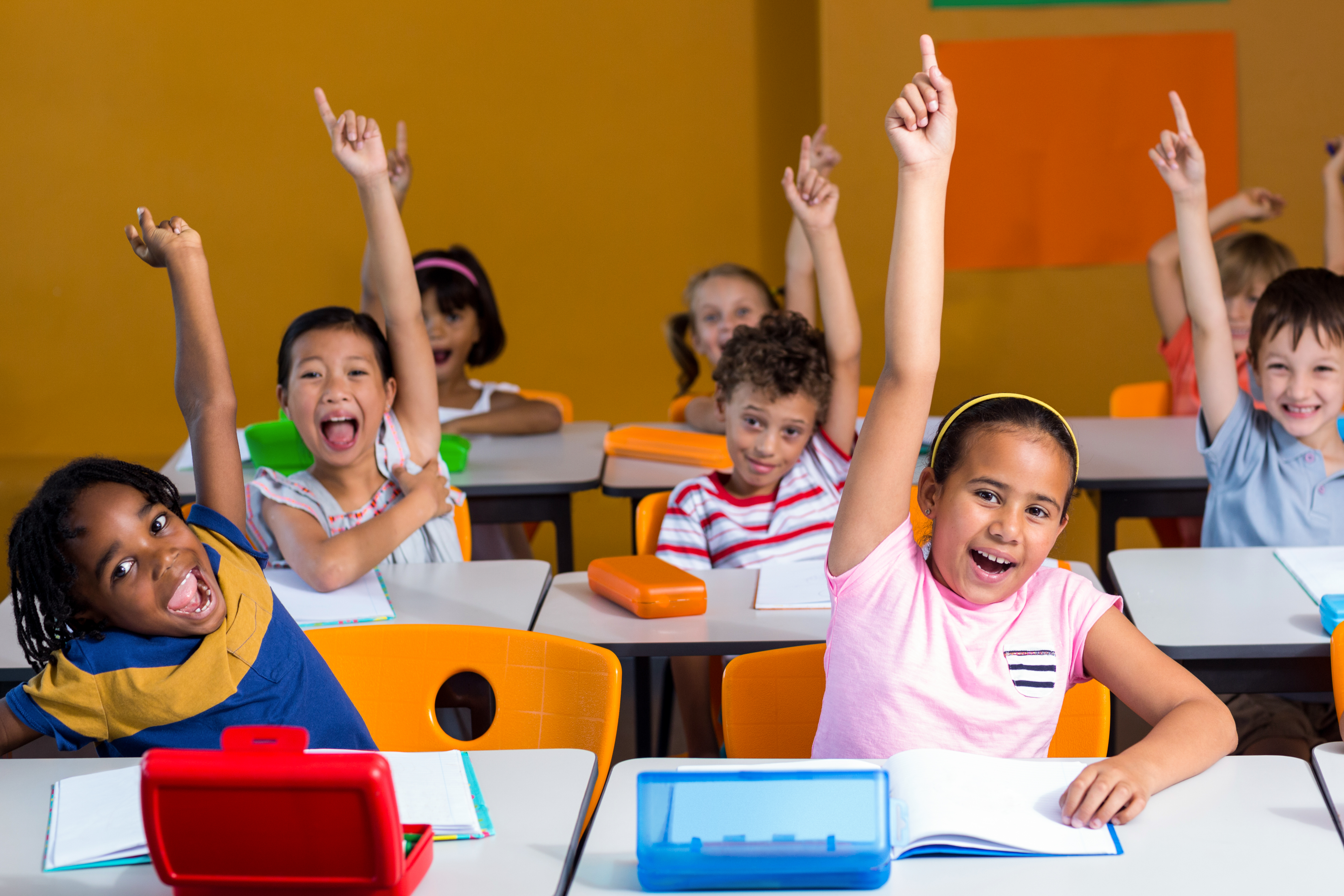 Smiling children in a classroom raising their hands
