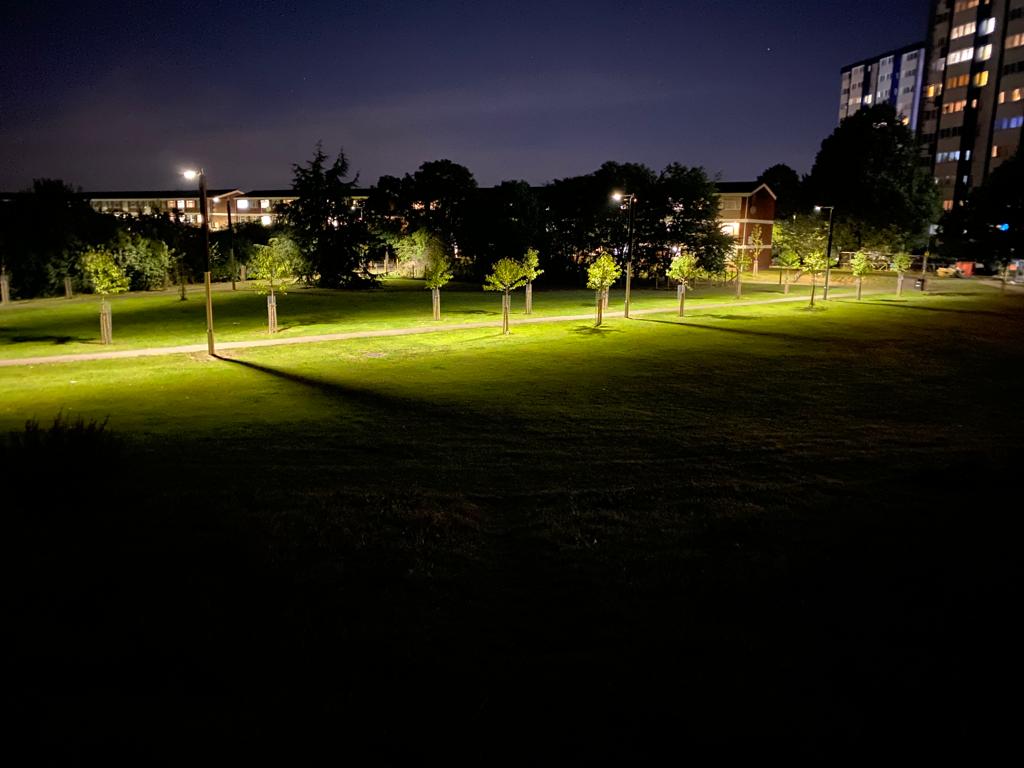 A park pathway at night lit up by streetlights.