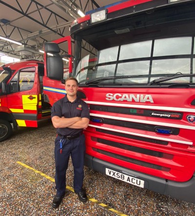 Stephen Balestrini stood in front of fire engine wearing fire uniform.