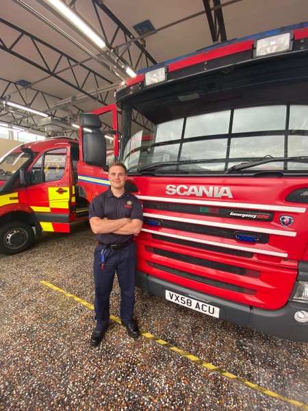 Stephen Balestrini stood in front of fire engine wearing fire uniform.