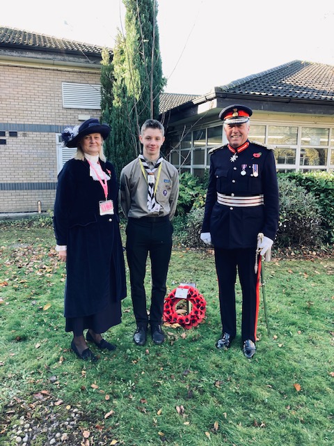 Three people stand with a poppy wreath