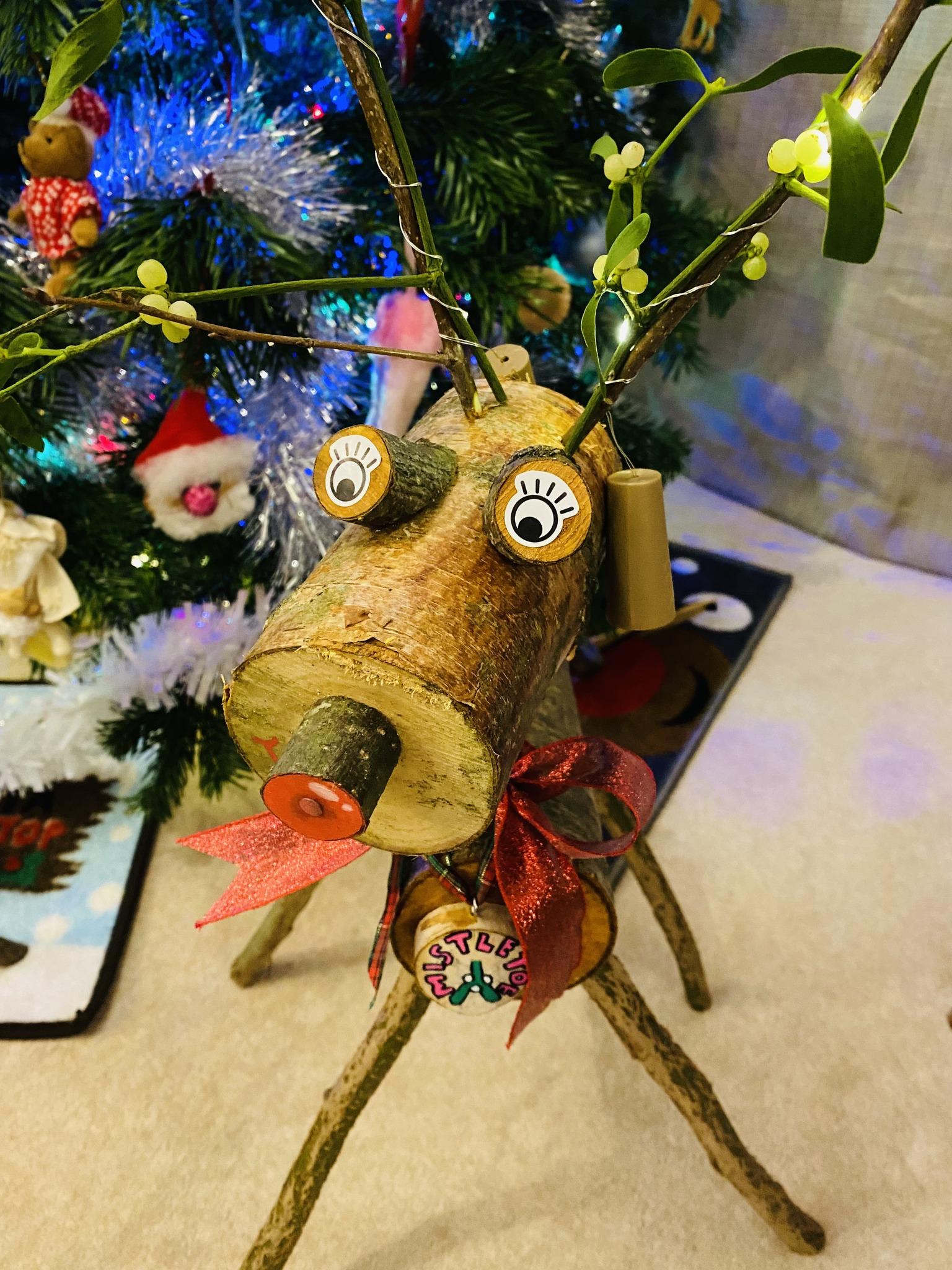 A homemade reindeer, covered in festive decoration, standing next to a Christmas tree