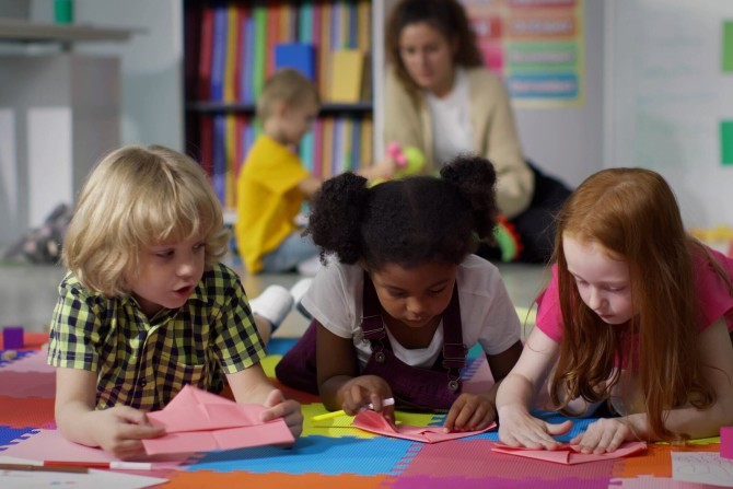 Three children making paper boats and talking to each other