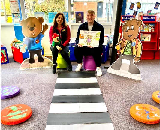 Two people leading a road safety education session, one holding a bear and the other an open book