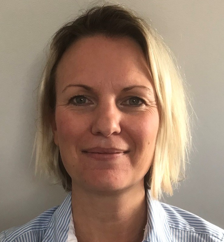 Sally Waldron, a slightly smiling woman in a blue shirt with short blond hair