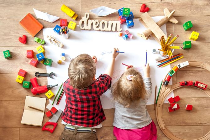 Two children colouring in with toys around them.