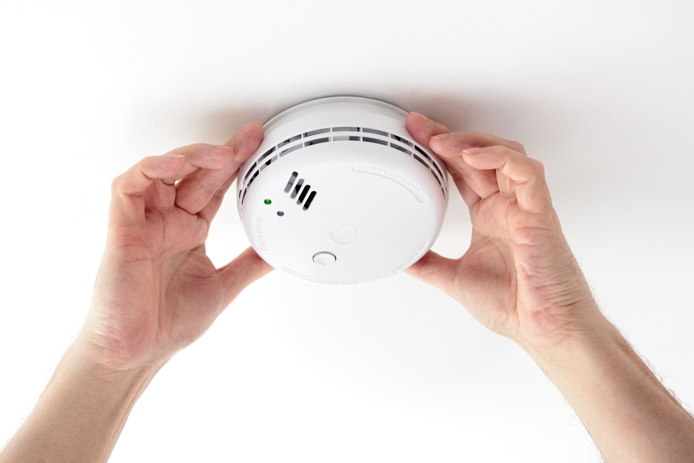 A photo of a pair of hands checking a smoke alarm on a ceiling