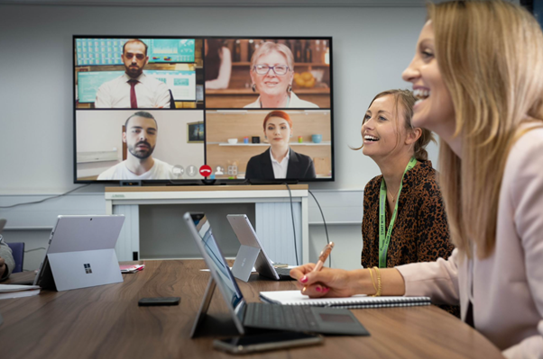 A photo of two people in a team meeting with people on the screen