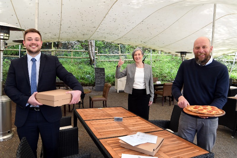 three people stood around an outdoor sheltered table holding food. The Antelope pub/restaurant