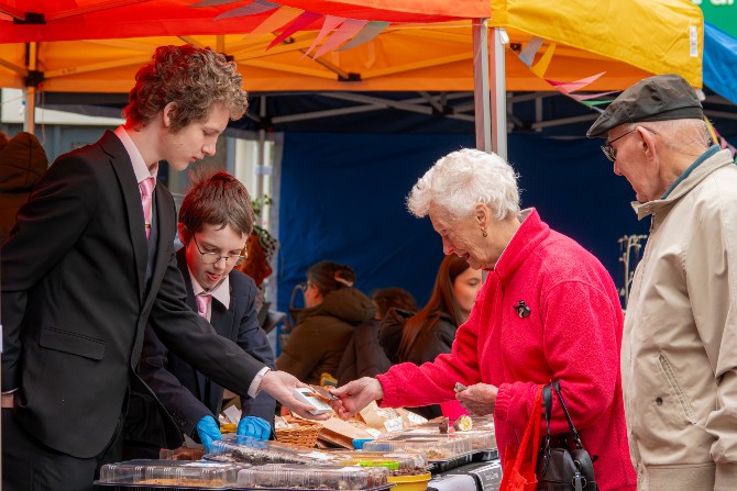 Two young adults showing their market stall goods to an elderly woman and man