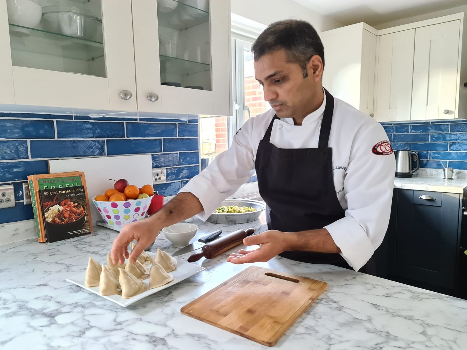 Male in chef whites and dark blue apron preparing samosas in a professional kitchen.