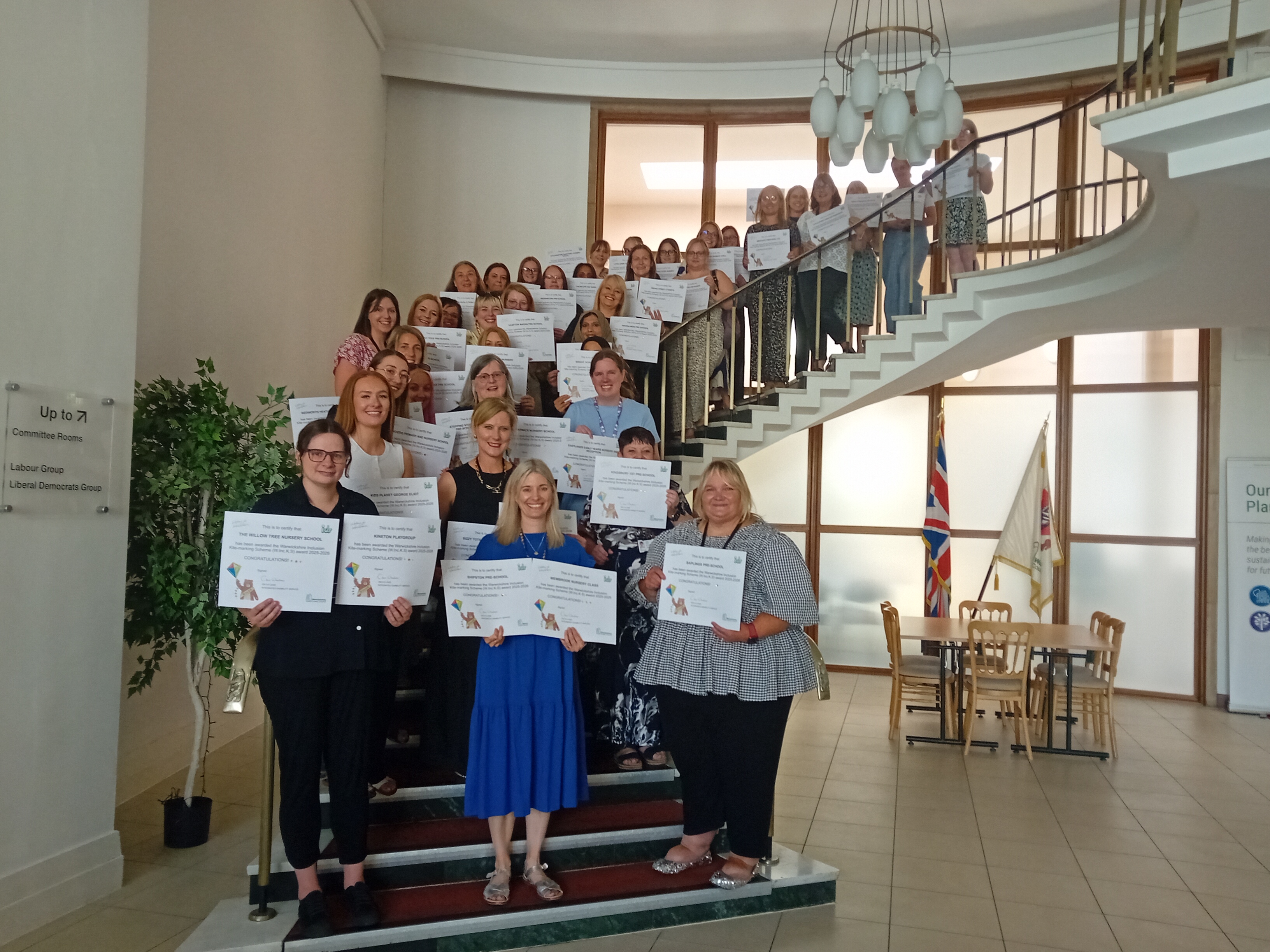 Representatives of early years settings with their WIncKS Awards 2025 certificates standing on the steps in the Antechamber at Shire Hall, Warwick