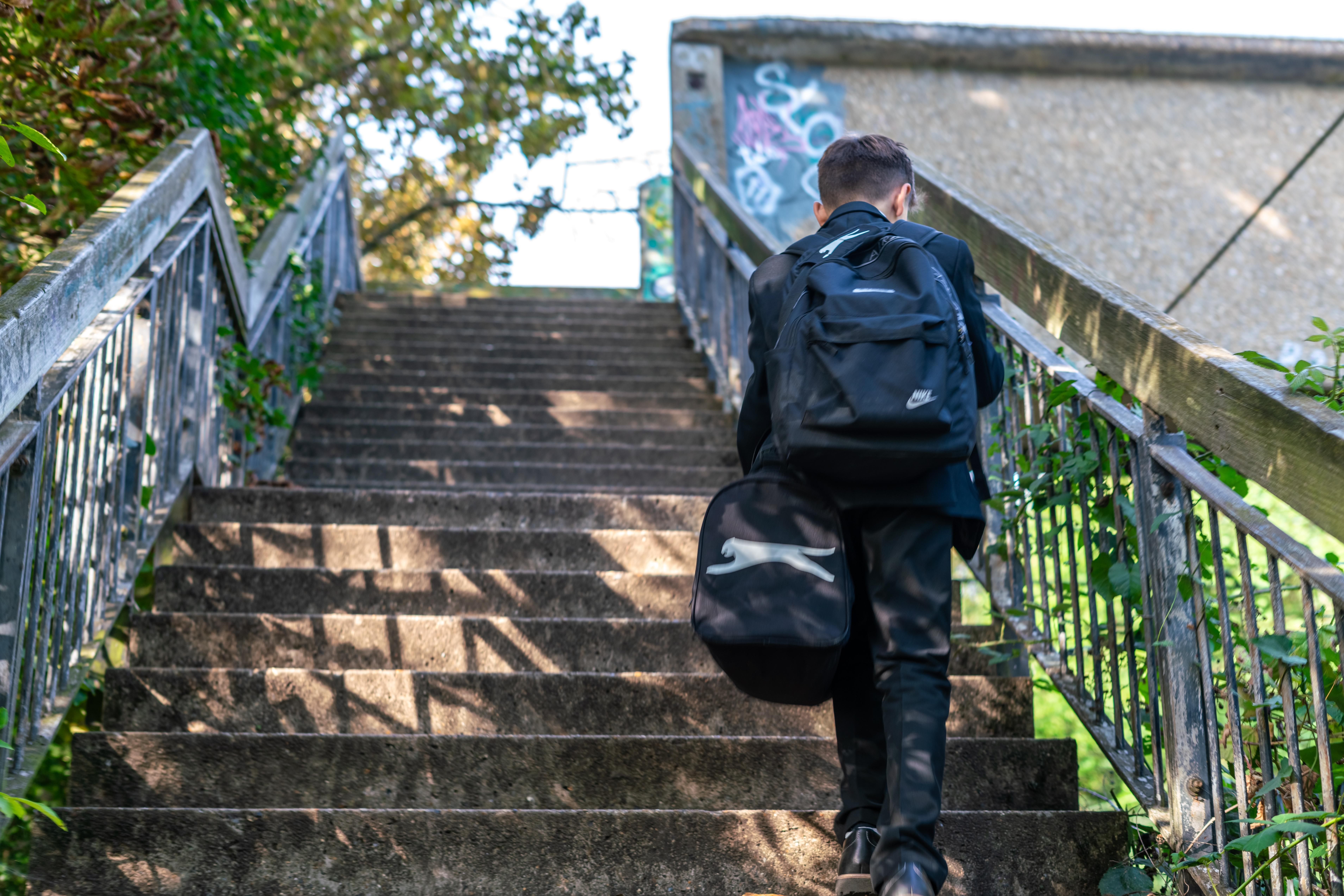 A boy walking up the right-hand side of a staircase, carrying school bags.