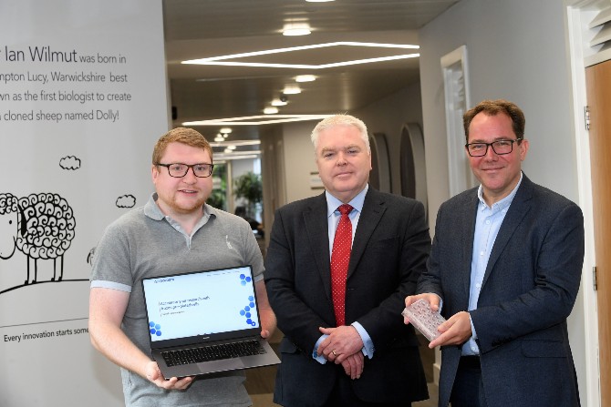 Three people standing with one holding a laptop