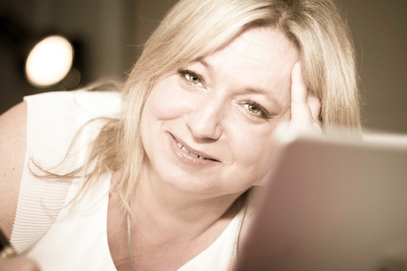 blonde female leaning on desk looking at the camera smiling.