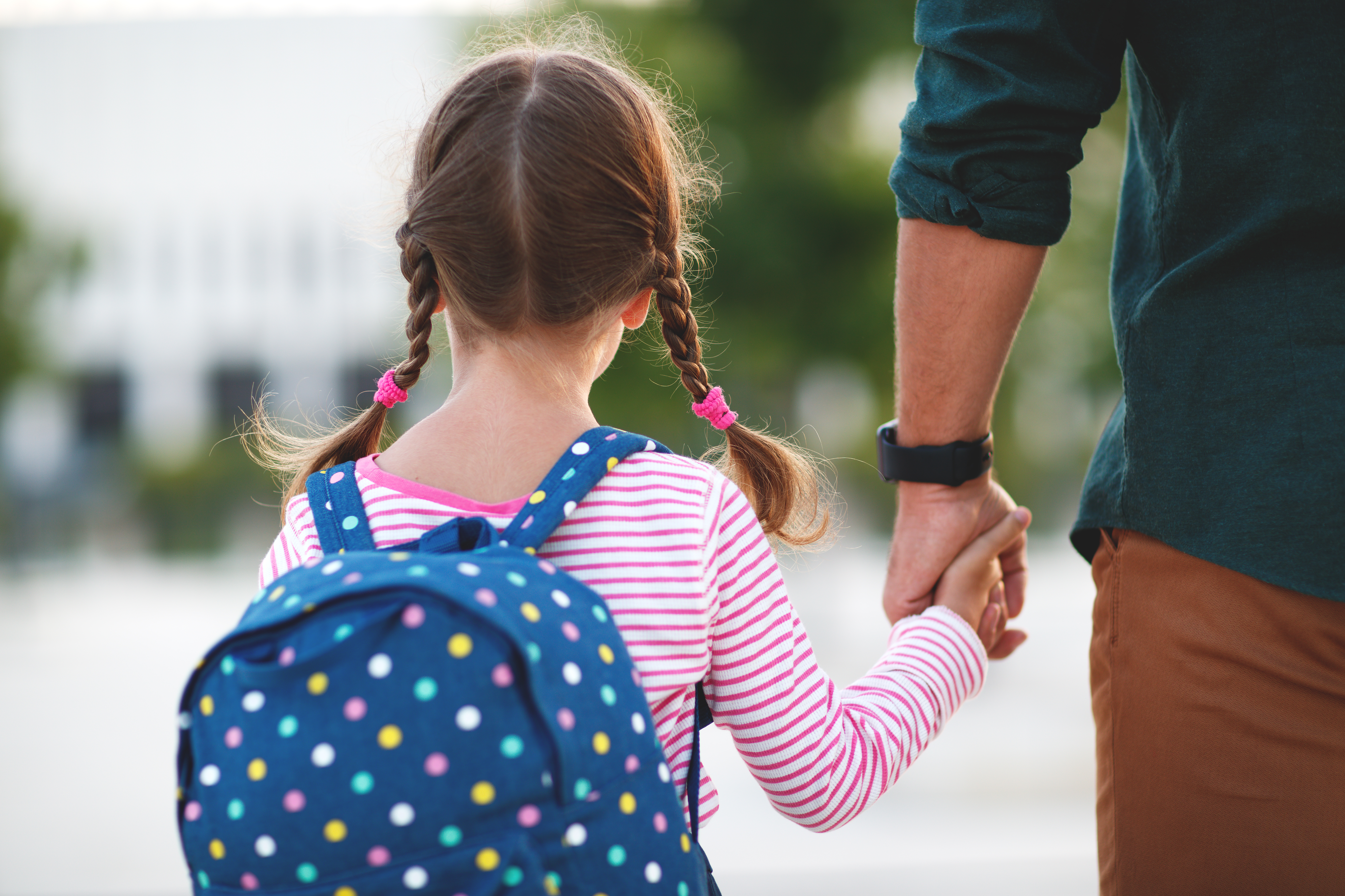 Girl holding hands with parent and wearing a backpack