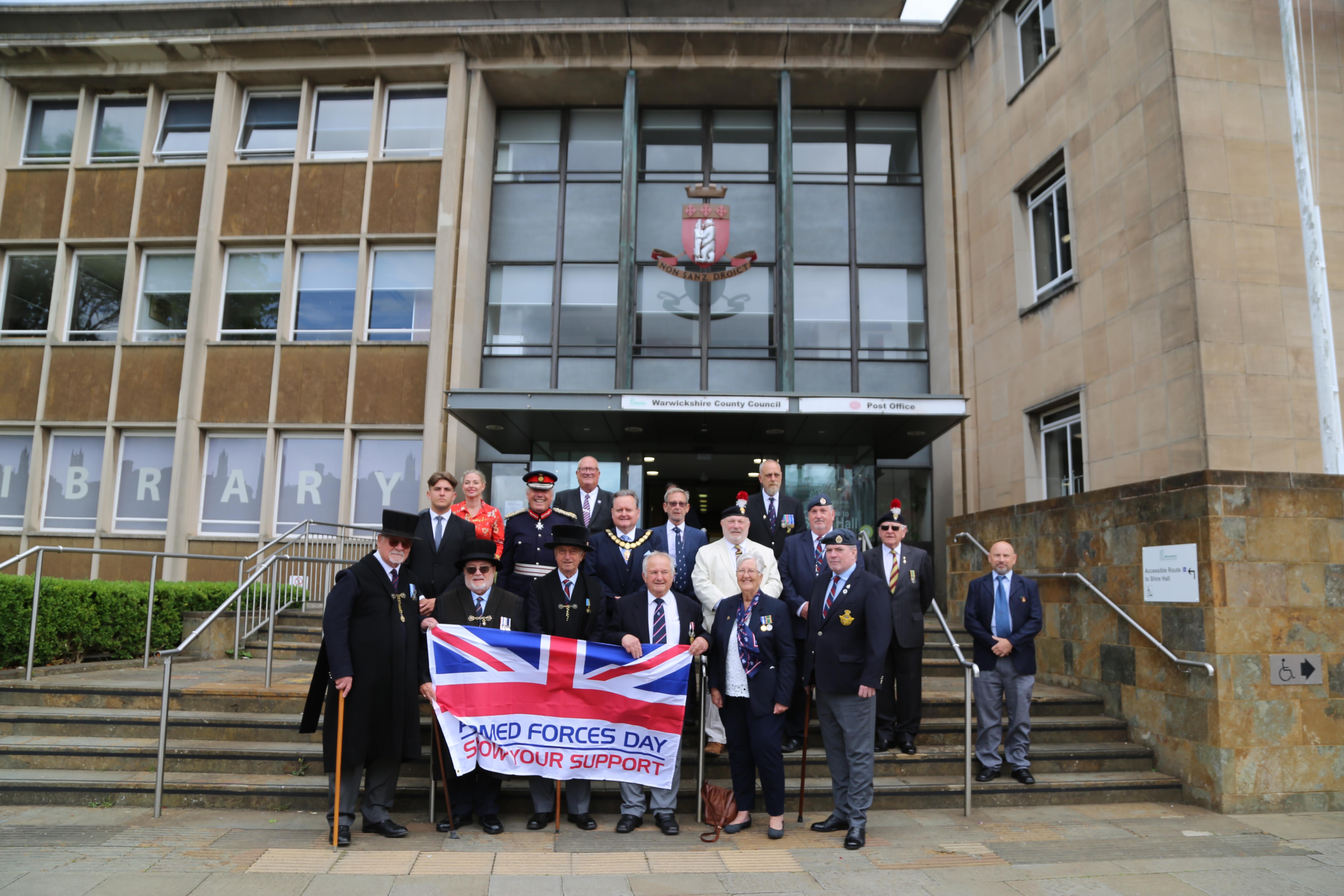 Veterans from the Veterans Contact Point, Warwickshire Fusiliers Association and branches of other veteran associations stood in front of stairs at entrance to Shire Hall.