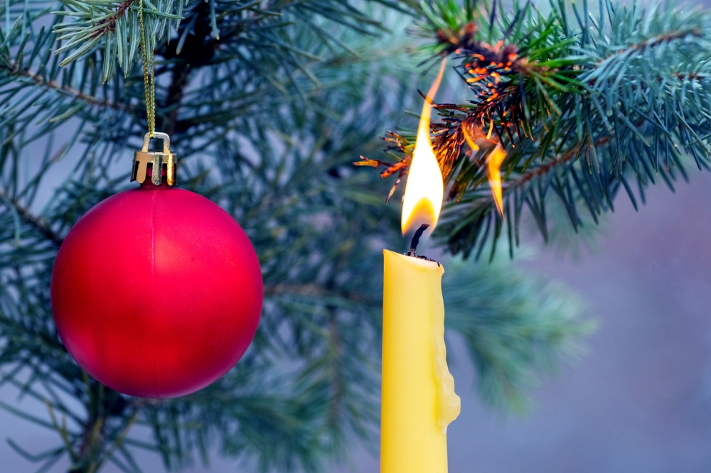 A Christmas tree branch being set alight by a candle