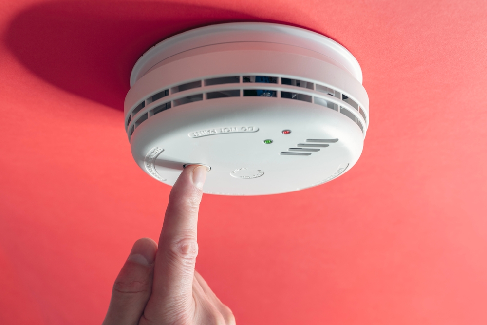 A hand pressing a button a smoke alarm to test it