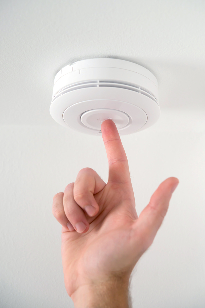 A hand with index finger extended to press button on smoke alarm to test it