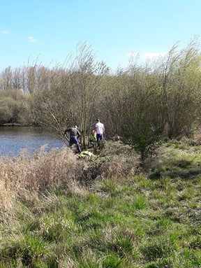 Two volunteers assist a Country Parks Ranger with habitat management by the side of a lake.